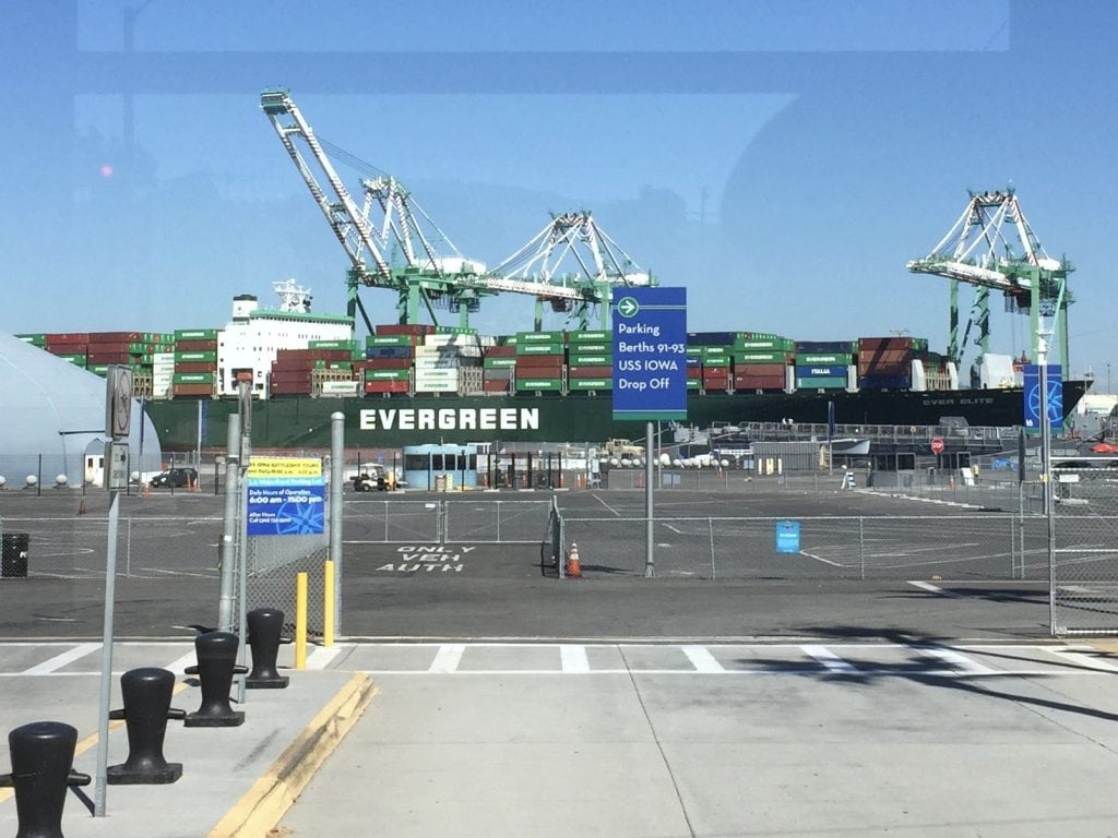 Large Evergreen container ship loaded with stacked cargo containers at the Port of Los Angeles, with cranes towering above the harbor.