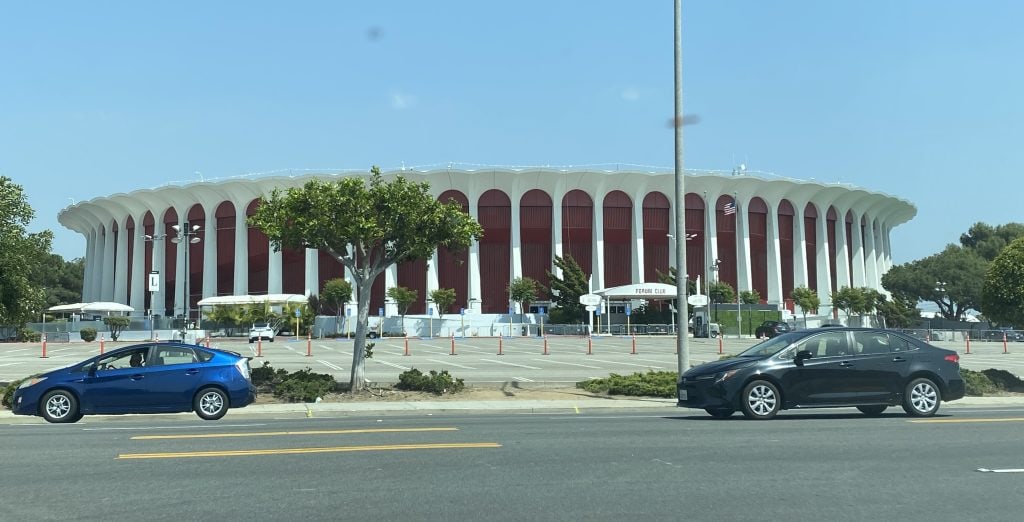 The Forum in Inglewood, California, with its white circular façade and red columns viewed from across the street.